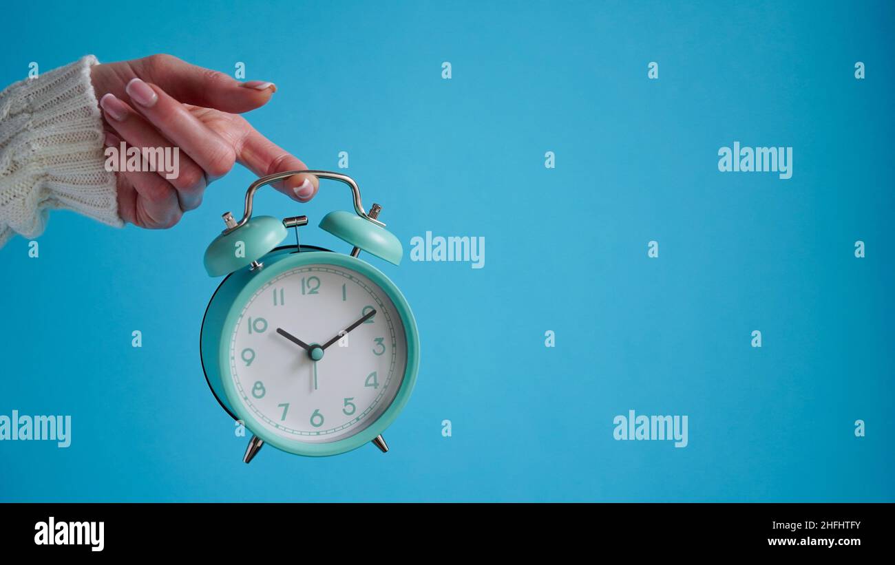 Gros plan de la main de la femme tenant le réveil rétro bleu fond bleu, l'heure sur l'horloge est dix heures dix minutes, 10:10.heure de se réveiller, tôt le matin.B Banque D'Images