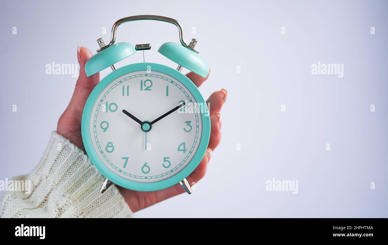 Gros plan de la main de femme tenant le réveil rétro bleu fond blanc,  l'heure sur l'horloge est dix heures dix minutes, 10:10.heure de se  réveiller, tôt le matin.BL Photo Stock -