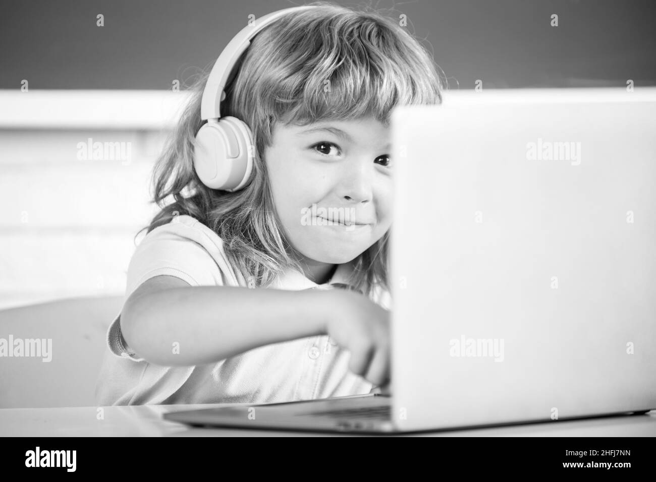 Gros plan portrait d'un enfant mignon dans un casque à l'aide d'un ordinateur portable et d'étudier en ligne avec un professeur de vidéoconférence à l'école. Banque D'Images