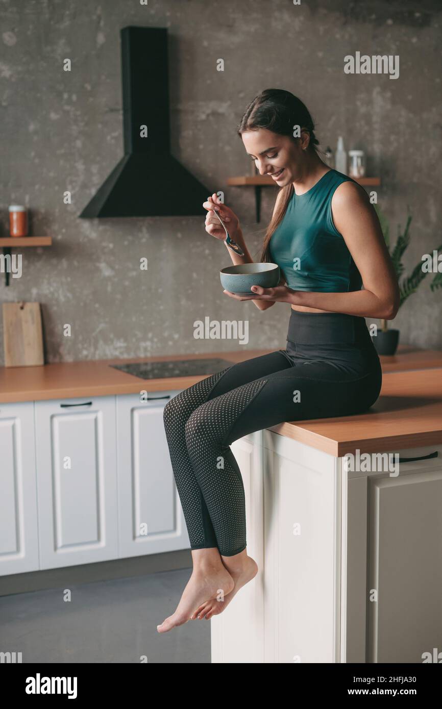 Femme caucasienne en vêtements de sport se reposant à la cuisine après l'exercice et manger un bol de porridge.Des aliments sains végétariens. Banque D'Images