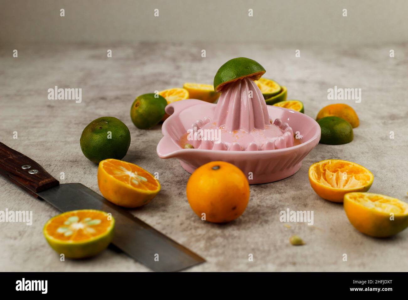 Presser le jus d'orange sur un presse-fruits en céramique manuel.Sur une table rustique avec un groupe de petites oranges. Banque D'Images