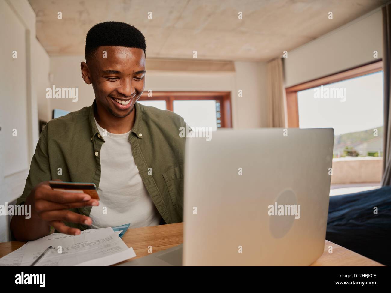 Jeune adulte noir homme excité de faire l'achat en ligne sur ordinateur portable dans l'appartement moderne. Banque D'Images Jeune adulte noir homme excité de faire l'achat en ligne sur ordinateur portable dans l'appartement moderne. Banque D'Images