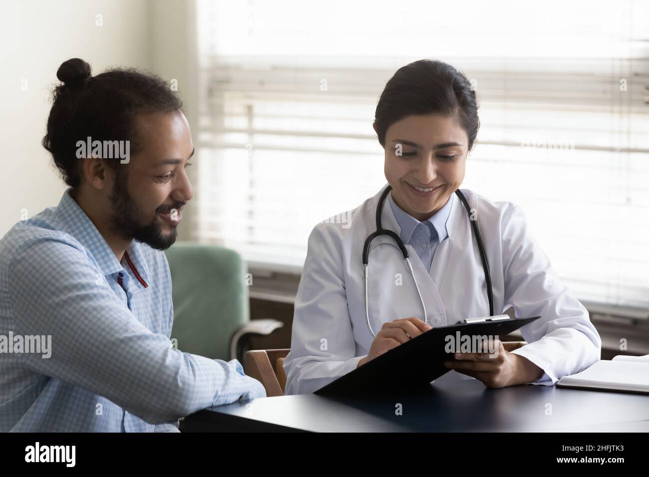 Joyeux jeune médecin indien communiquant avec le patient. Banque D'Images