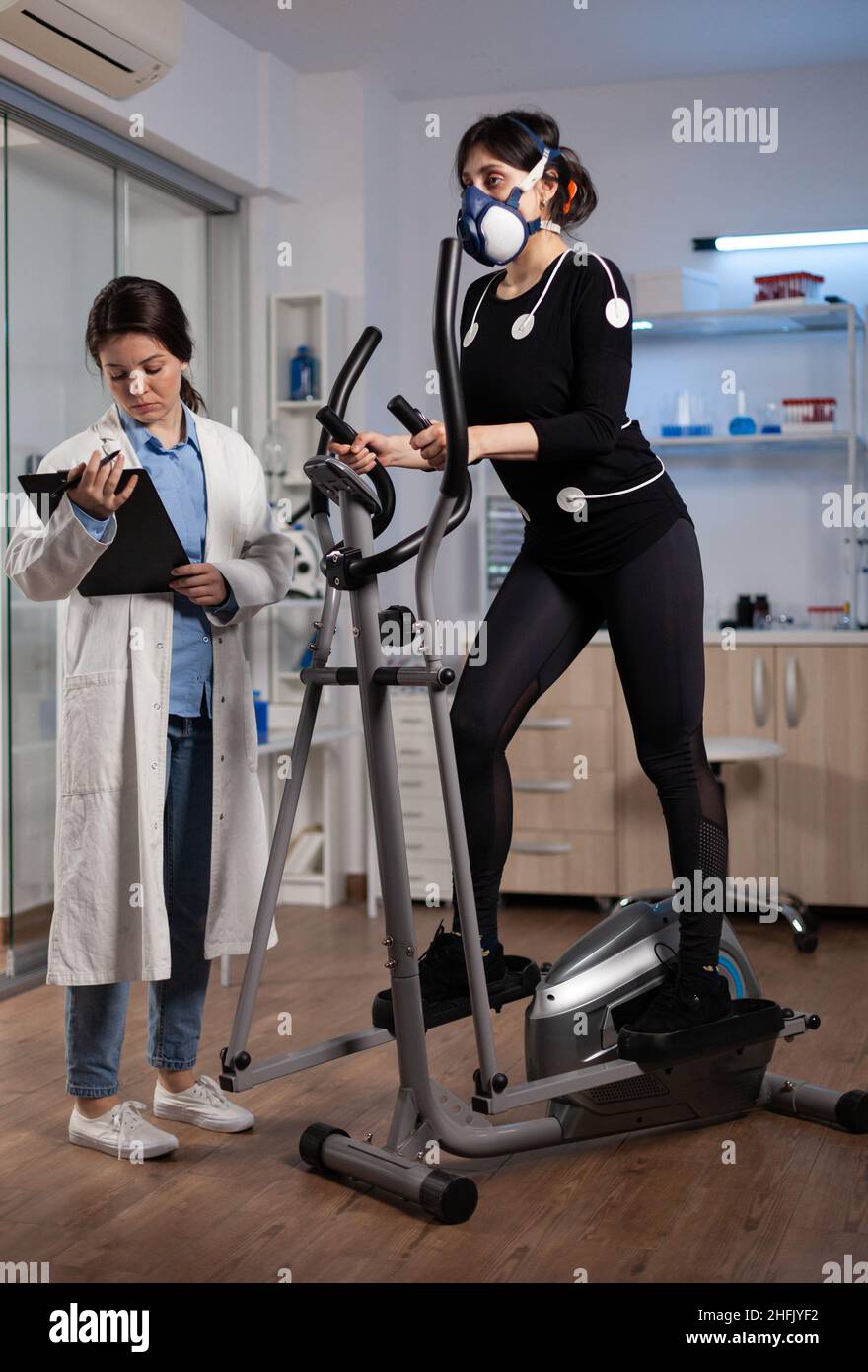 Athlète coureur femme portant des électrodes médicales travaillant à l'endurance du corps faisant l'exercice cardio en laboratoire tandis que chercheur scientifique surveillant la fréquence cardiaque.Médecin médecin médecin examinant les données EKG Banque D'Images