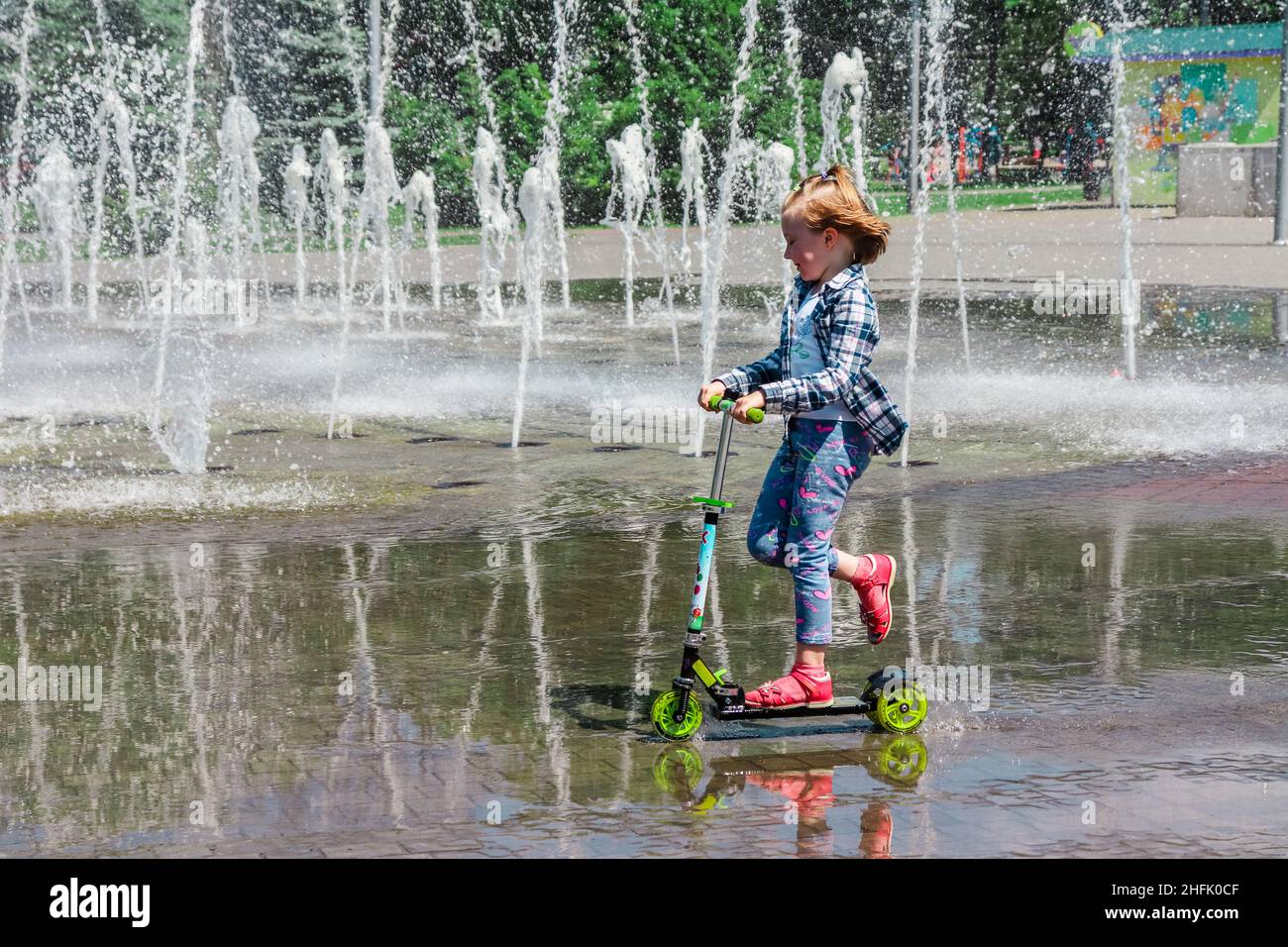 Ukraine - 26 mai 2018.Une fille fait un scooter dans une flaque à côté de la fontaine. Banque D'Images