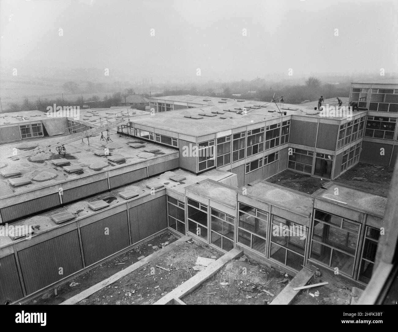 County High School, Gedling Road, Arnold, Gedling, Notinghamshire,23/02/1959.Vue du sud-ouest depuis une fenêtre supérieure dans le bloc scientifique de l'Arnold County High School, montrant des ouvriers qui répandaient du gravier sur les toits des bâtiments de l'école inférieure.Les travaux ont commencé sur le site en mars 1958 et les travaux de construction ont été achevés pour la nouvelle période scolaire en septembre 1959.L'école de grammaire co-éducative a accueilli 720 élèves.Au milieu de 1960s, une autre école a été construite à proximité et, en 1974, les deux ont été fusionnées en une école complète.Les bâtiments scolaires construits par Laing ont finalement été démolis en 2017. Banque D'Images