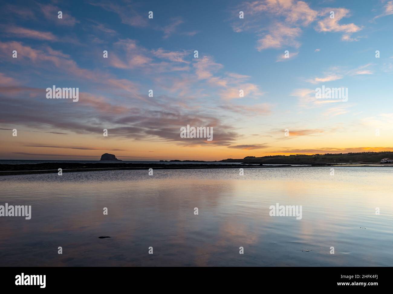 North Berwick, East Lothian, Écosse, Royaume-Uni, 17th janvier 2022.Météo au Royaume-Uni : lever du soleil au-dessus du Firth of Forth avec Bass Rock à l'horizon de la mer et nuages roses à l'aube reflétés dans l'eau de mer de la piscine à marée Banque D'Images