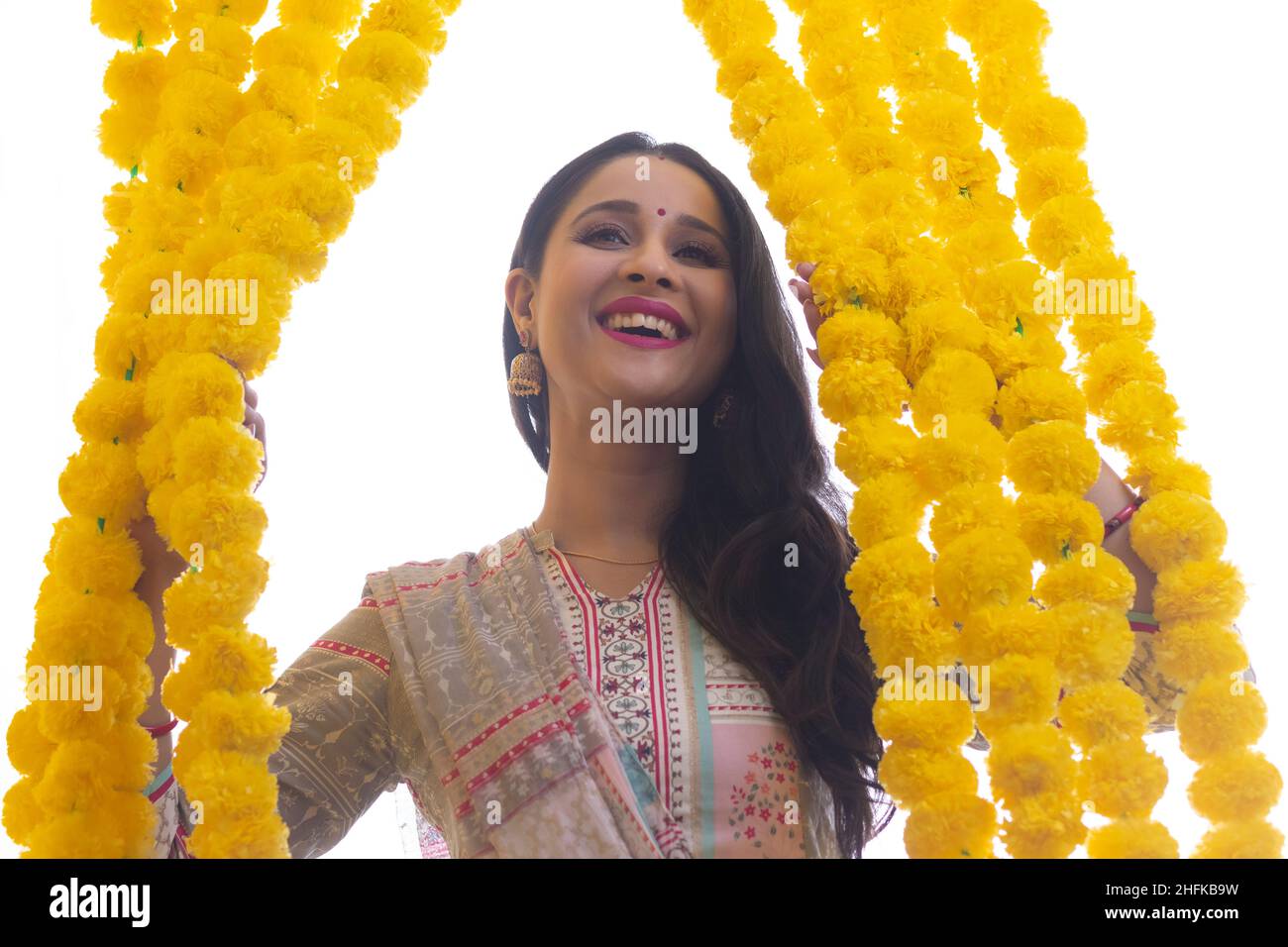 Une femme habillée de vêtements traditionnels debout au milieu de la décoration festive des guirlandes de fleurs. Banque D'Images