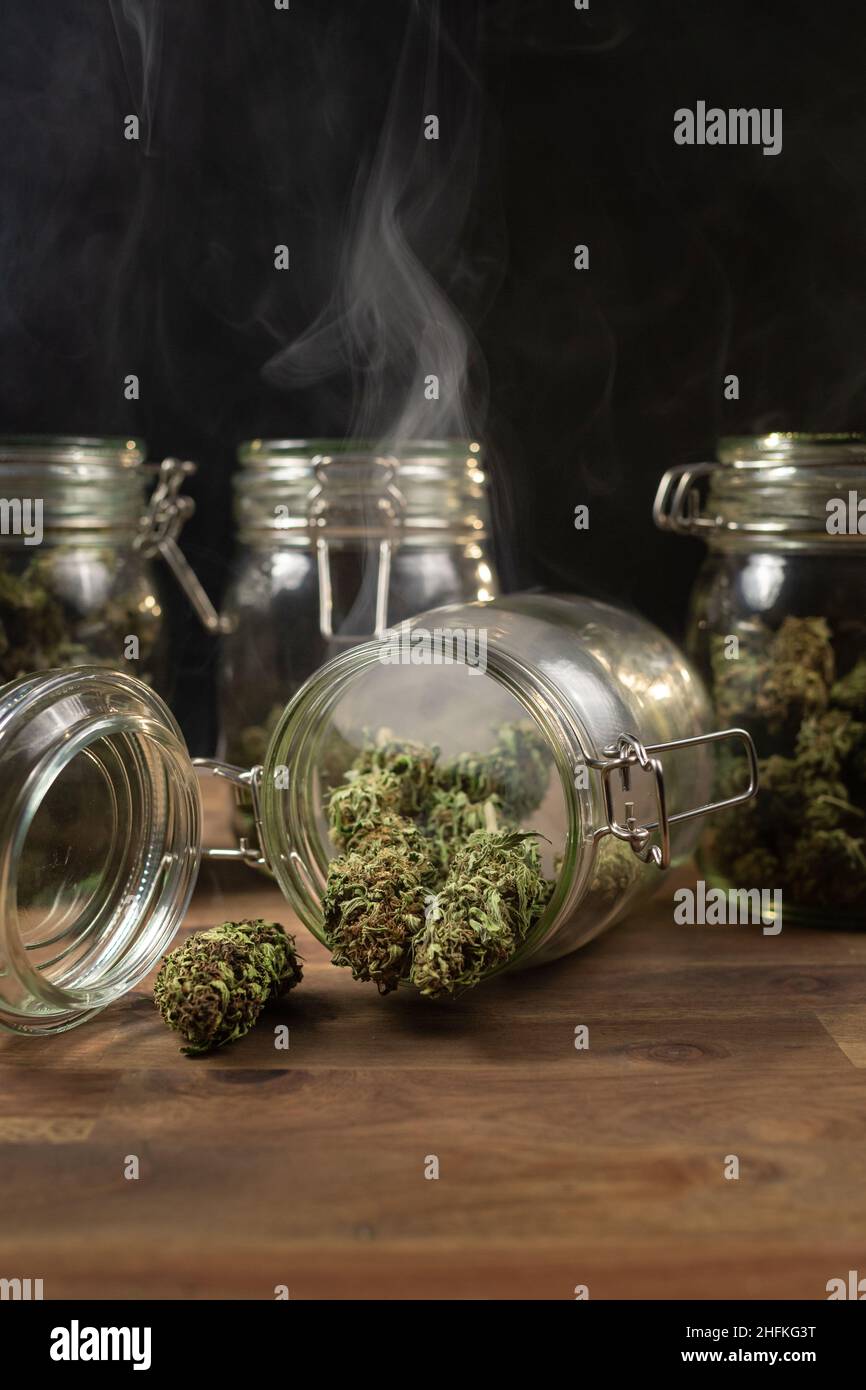 Prise verticale de pots de conservation en verre, remplis de bourgeons de cannabis, dans un nuage de fumée. Banque D'Images