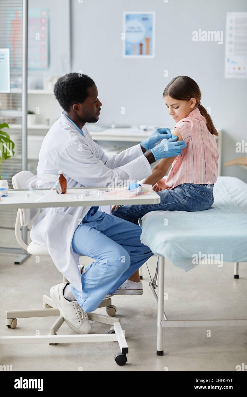 Portrait vertical de la petite fille courageuse se faisant vacciner contre le COVID-19 dans une clinique de vaccination des enfants Banque D'Images