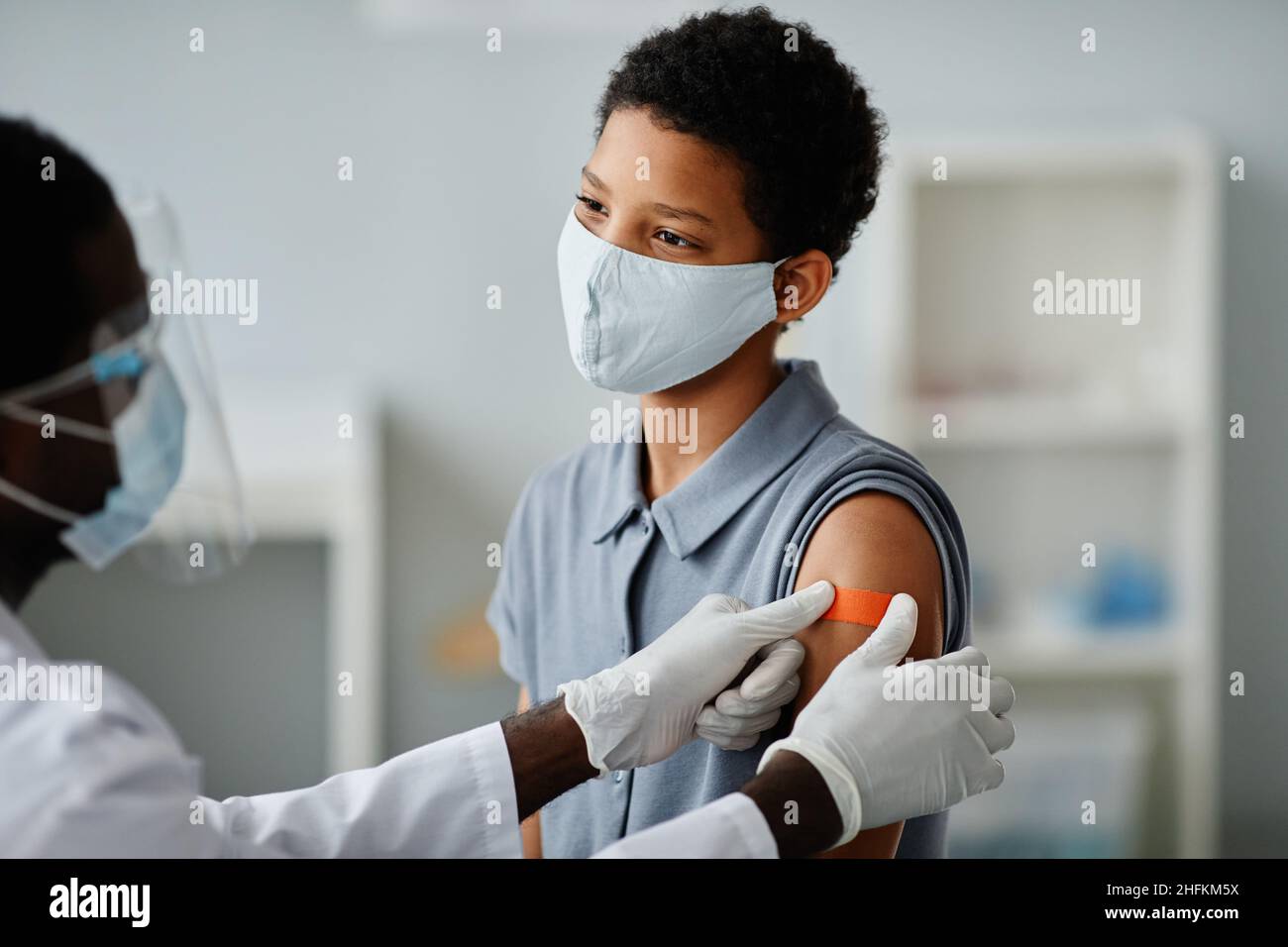 Portrait d'une jeune fille afro-américaine courageuse se faisant vacciner dans une clinique de vaccination des enfants avec un médecin mettant du plâtre stérile sur l'épaule Banque D'Images