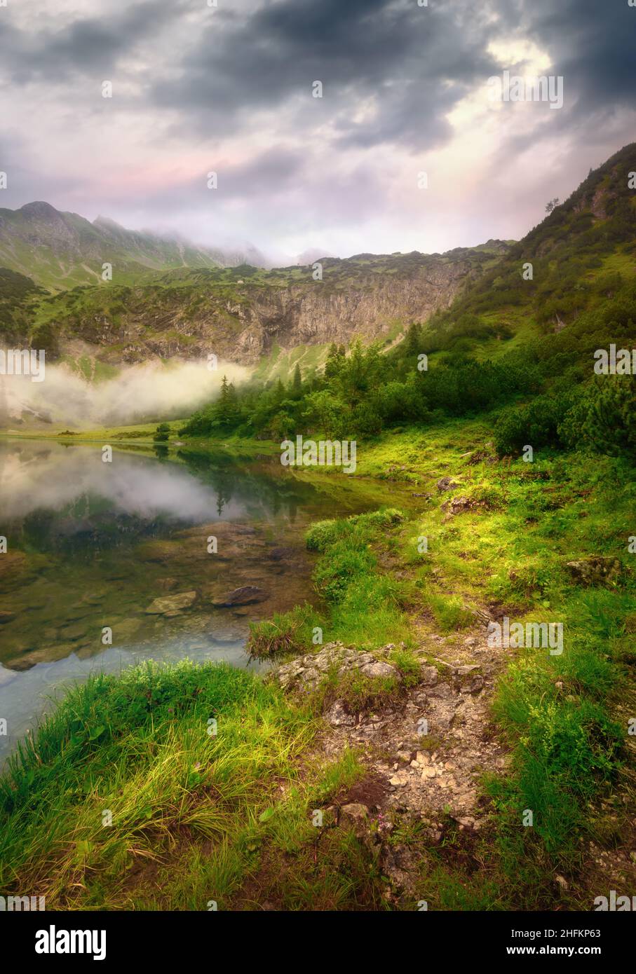 Magnifique sentier au bord d'un lac de montagne dans une lumière spectaculaire avec des nuages sombres Banque D'Images