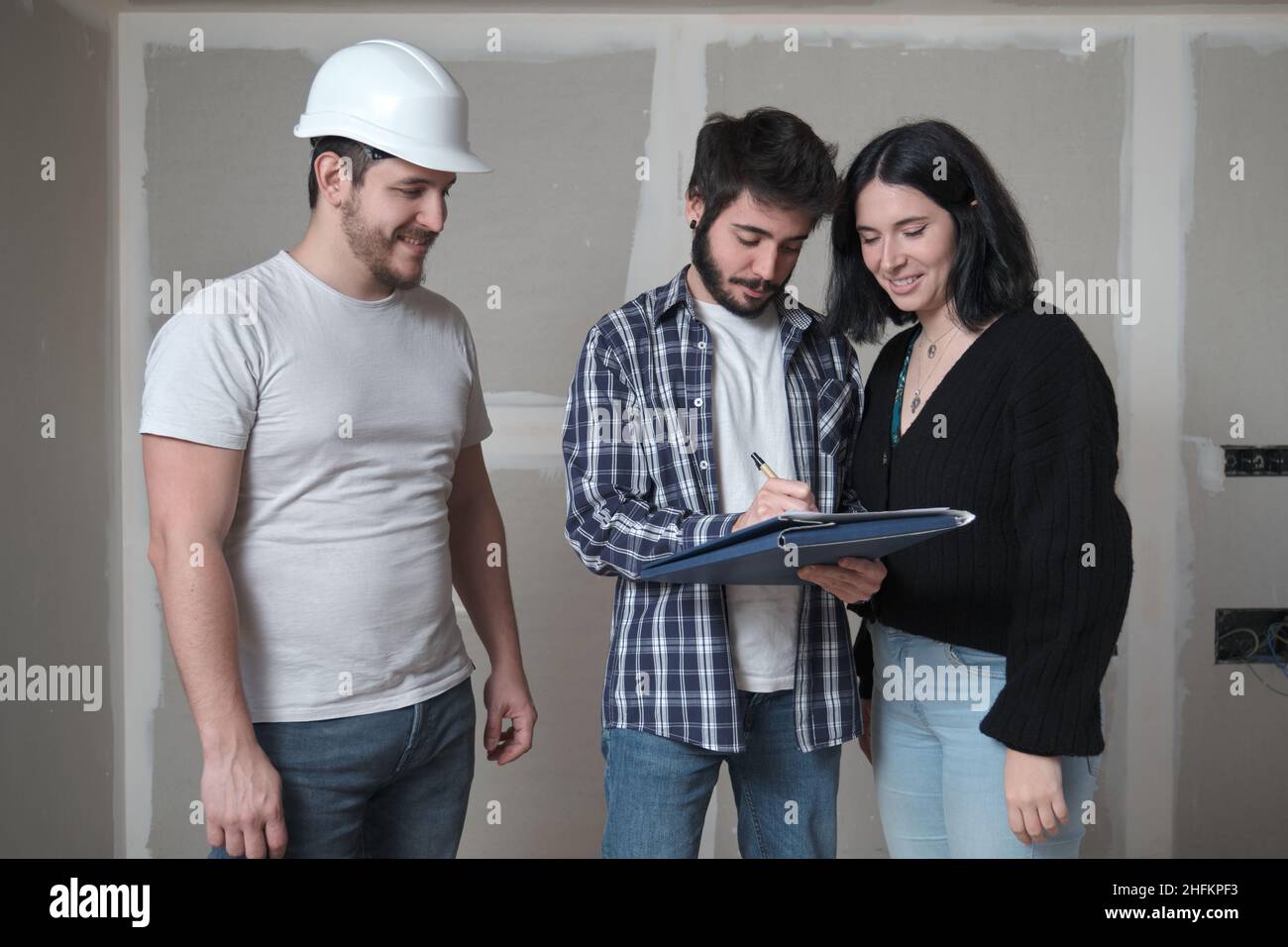 Mari d'un jeune couple signant un document pour acheter la maison en construction. Banque D'Images