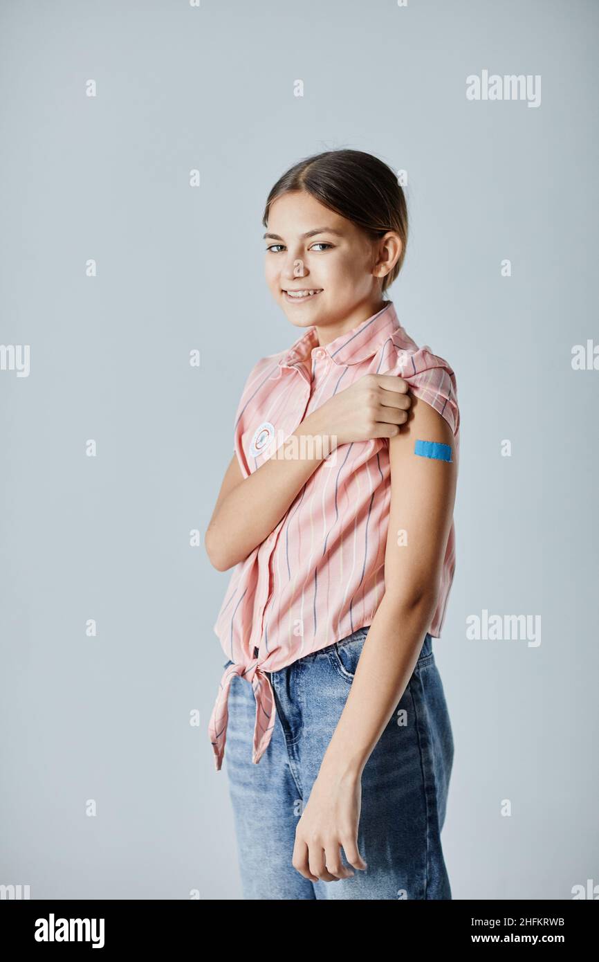 Portrait vertical d'une jeune fille adolescente mignonne montrant une zone d'épaule et souriant à l'appareil photo après avoir été vaccinée Banque D'Images