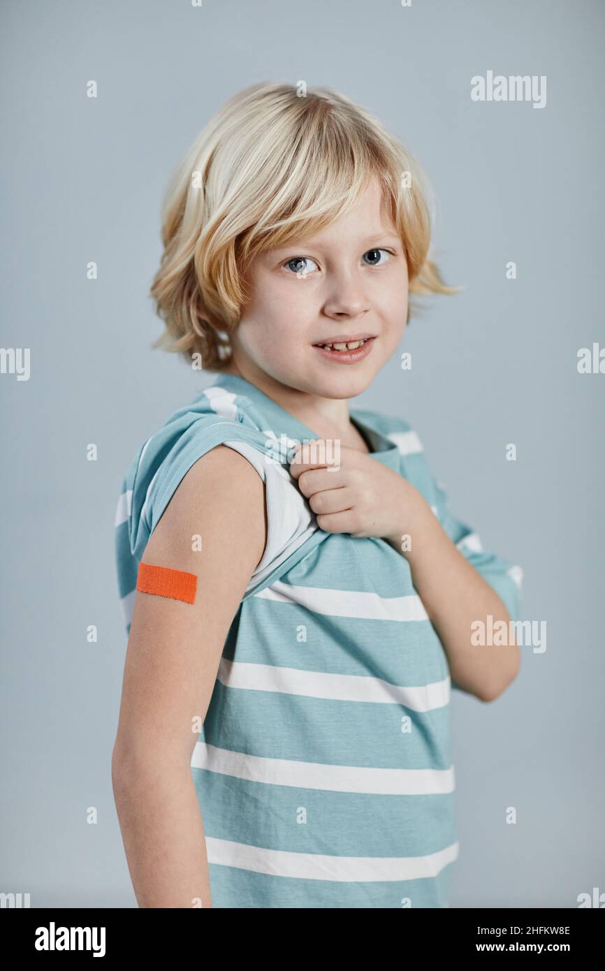 Portrait vertical d'un garçon mignon montrant une zone d'épaule et souriant à l'appareil photo après avoir été vacciné Banque D'Images
