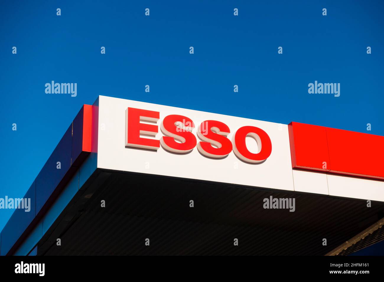 La station-service Esso parcourt la signalisation sur le toit contre le ciel bleu clair. Banque D'Images