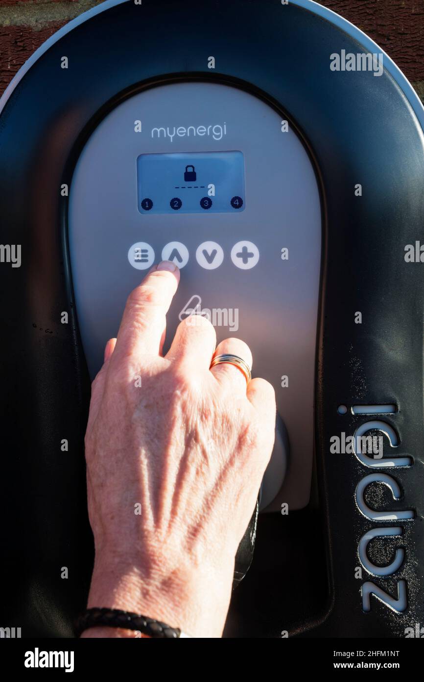 Femme entrant PIN pour déverrouiller un chargeur de voiture électrique Zappi fixé au mur extérieur d'un garage privé.Fonction de sécurité pour éviter le vol d'électricité. Banque D'Images
