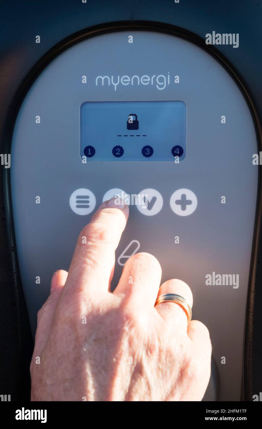 Femme entrant PIN pour déverrouiller un chargeur de voiture électrique Zappi fixé au mur extérieur d'un garage privé.Fonction de sécurité pour éviter le vol d'électricité. Banque D'Images