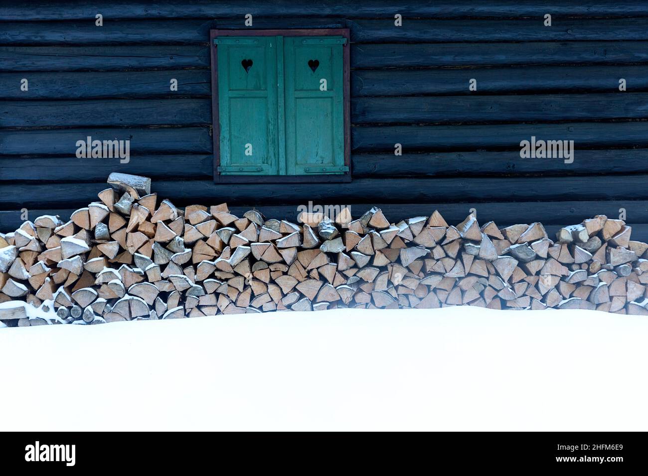 Une fenêtre avec des volets verts avec des coeurs sur une ancienne cabine alpine en hiver avec de la neige et du bois de chauffage Banque D'Images