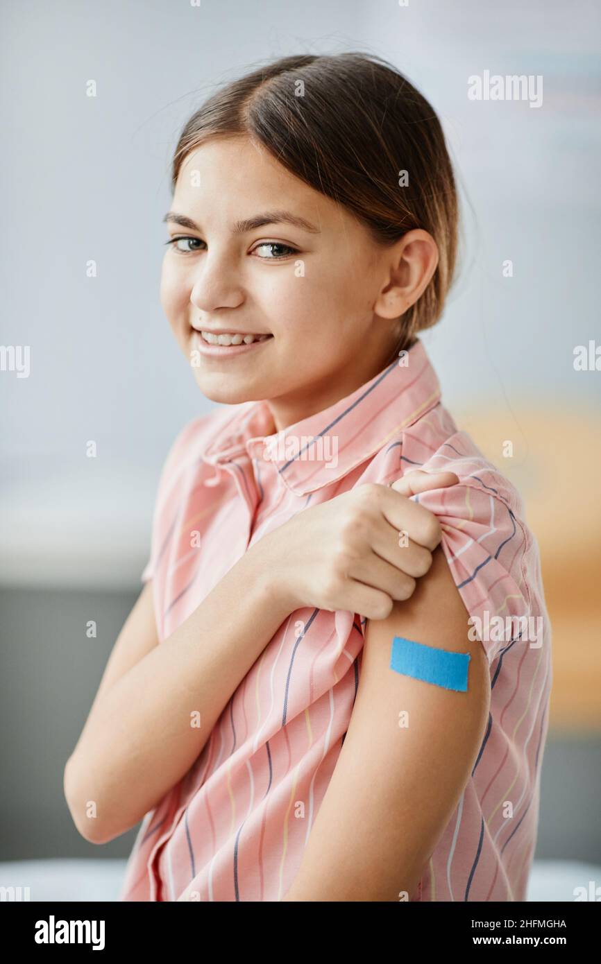Portrait vertical de petite fille souriante montrant l'épaule avec le plâtre après avoir été vaccinée contre le covid 19 Banque D'Images