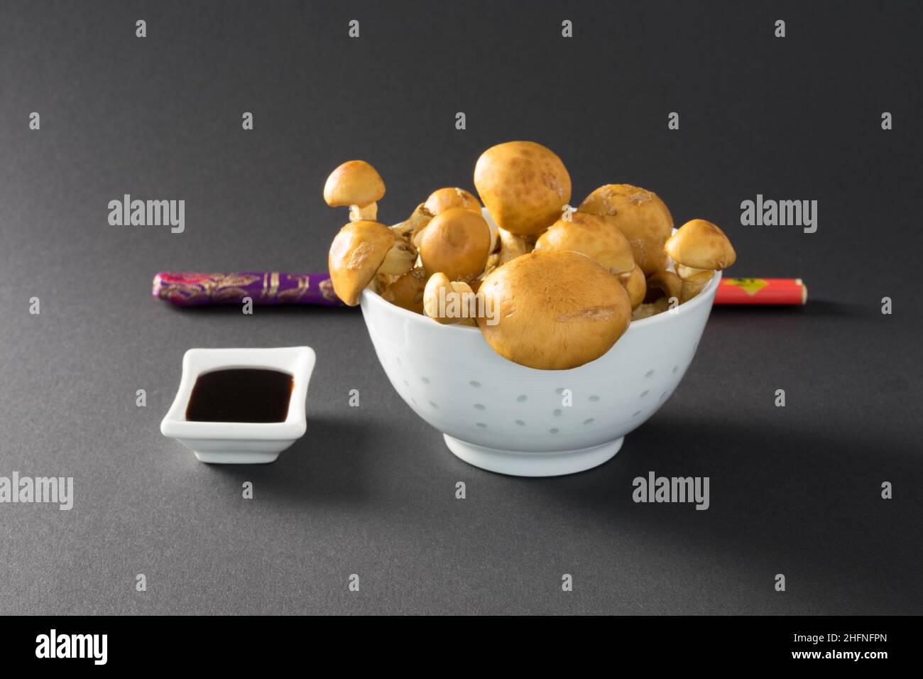 Délicieux champignons à chapeau doré sur fond noir dans un bol blanc avec un bol blanc de sauce soja, frais et crus, gros plan Banque D'Images