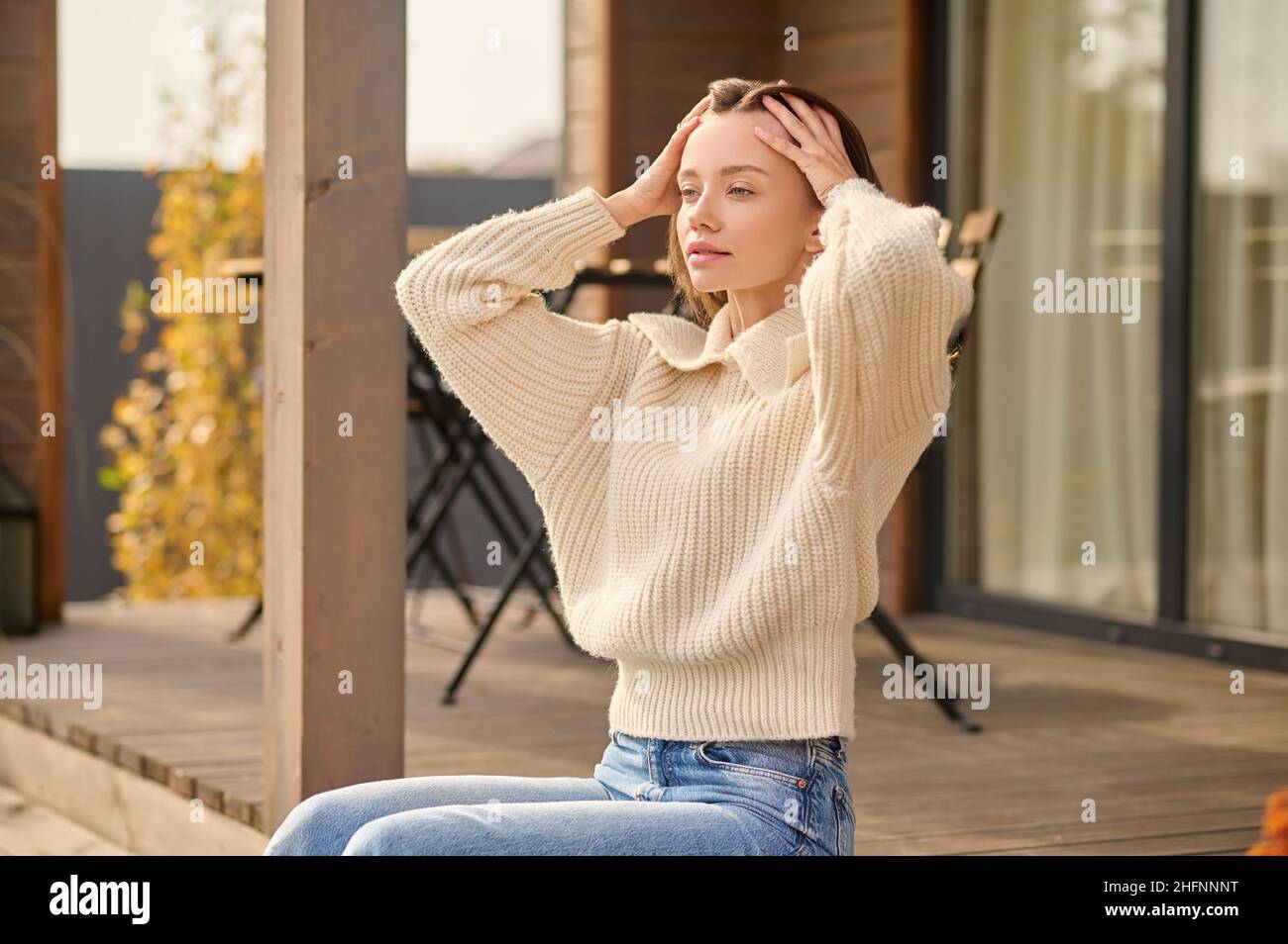 Femme touchant les cheveux assis sur le porche de la maison de campagne Banque D'Images