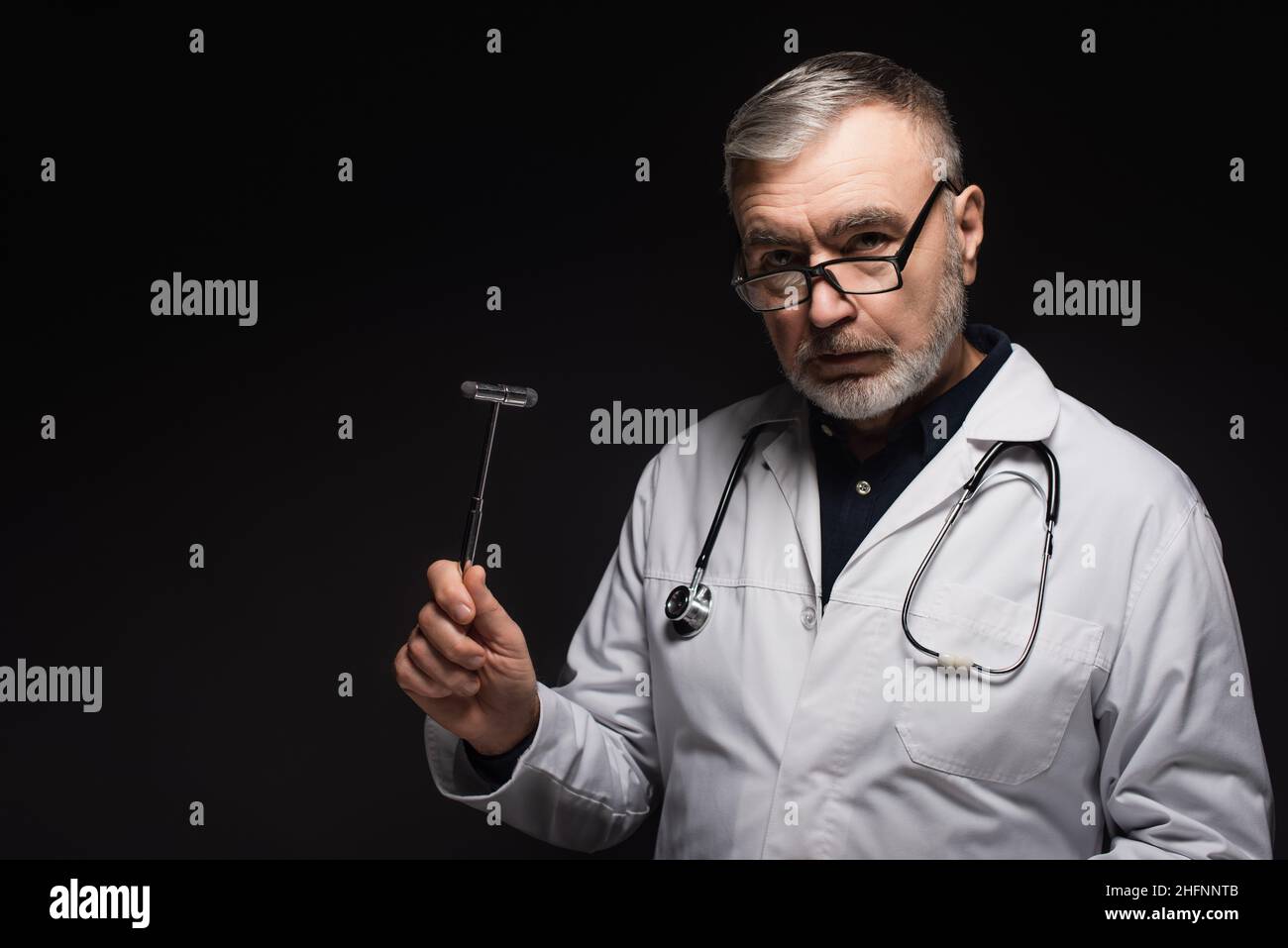 neurologue senior dans les lunettes tenant le malléus réflexe et regardant la caméra isolée sur noir Banque D'Images