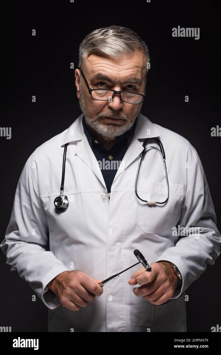 neurologue senior avec malléus réflexe et stéthoscope regardant la caméra isolée sur noir Banque D'Images