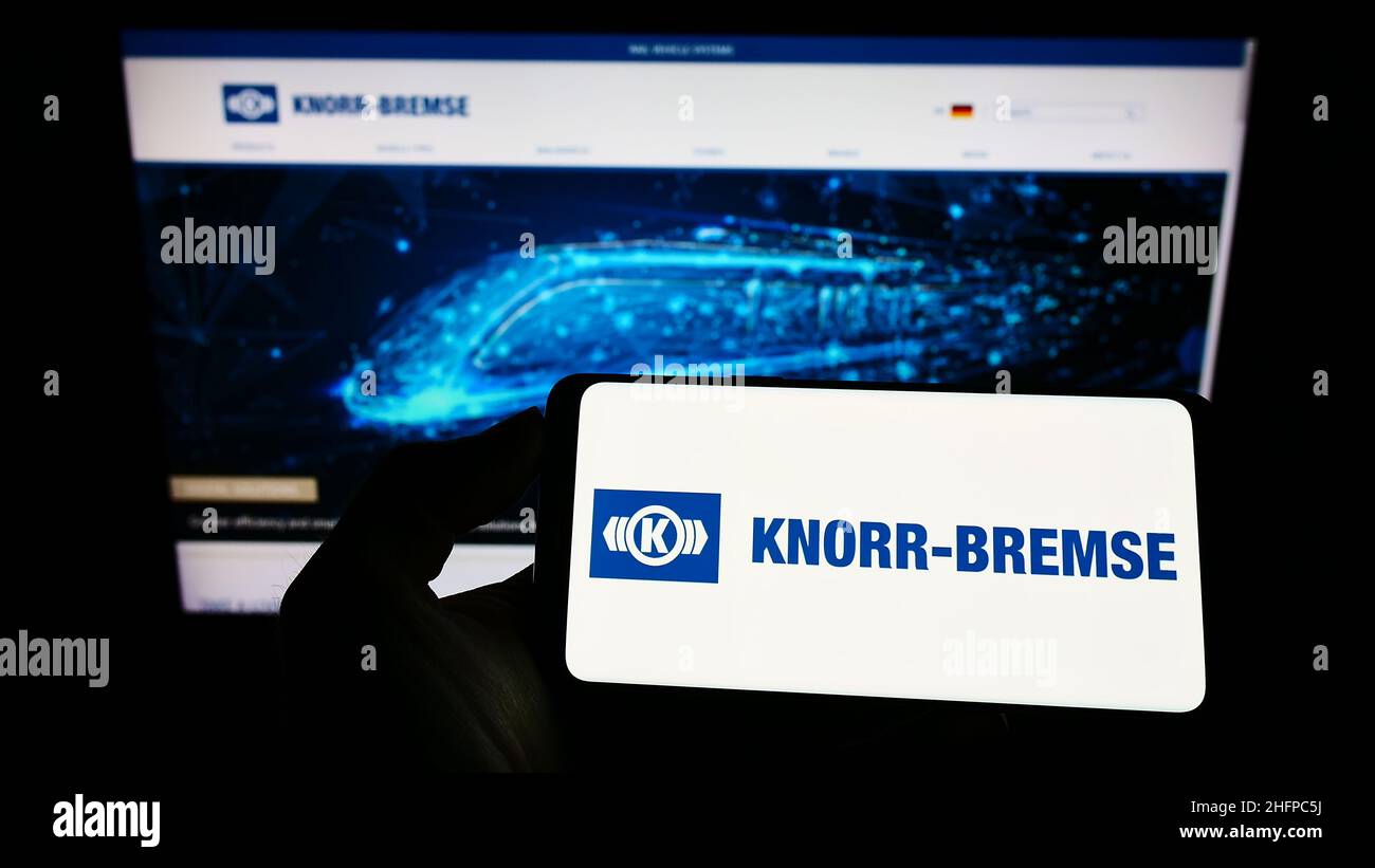 Personne tenant un téléphone portable avec le logo de la société allemande de fabrication Knorr-Bremse AG à l'écran en face de la page web d'affaires.Mise au point sur l'affichage du téléphone. Banque D'Images