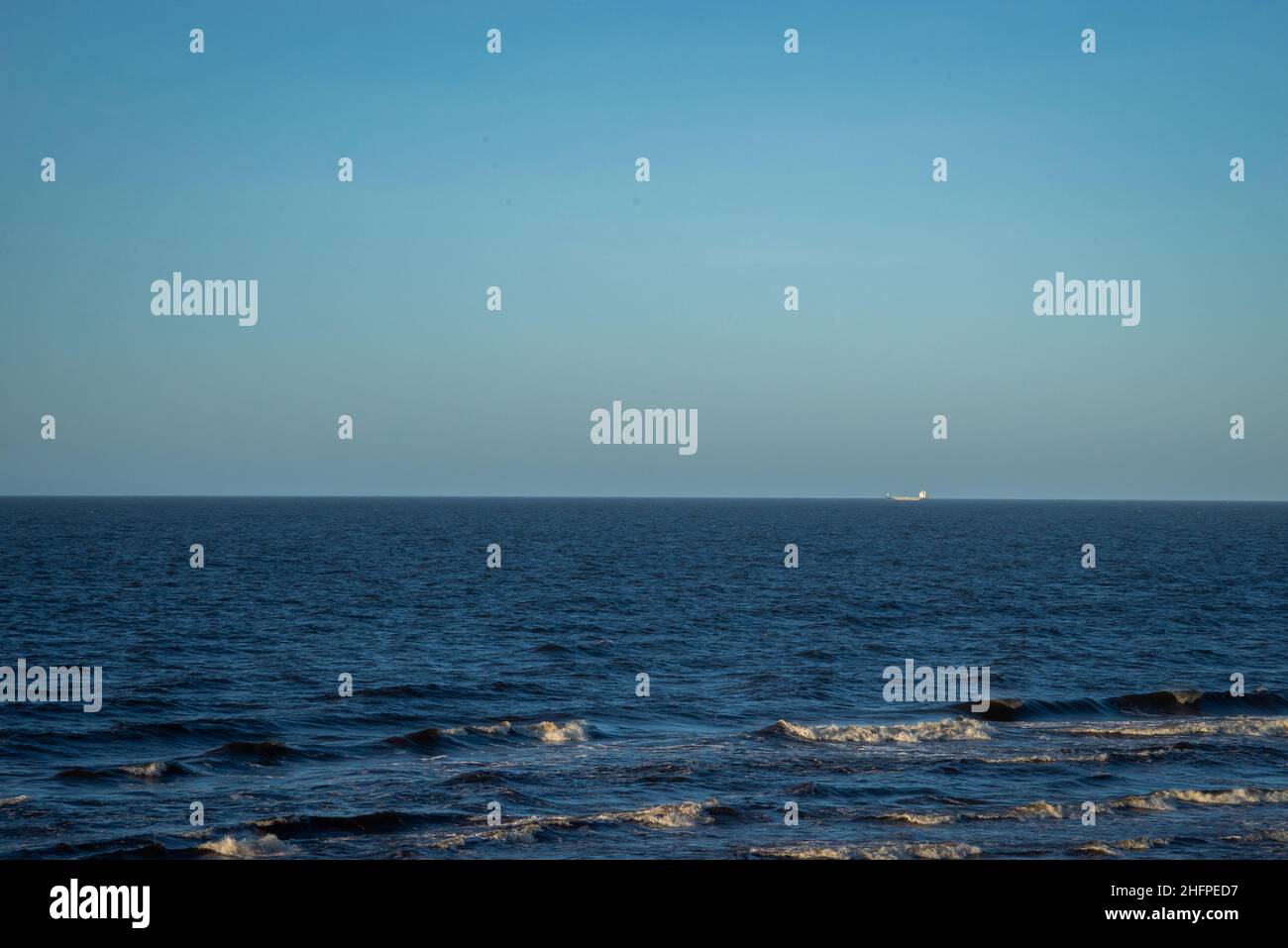Paysage de mer avec eau bleue et vagues avec mousse blanche.Un navire de transport peut être vu à la distance à l'horizon. Banque D'Images