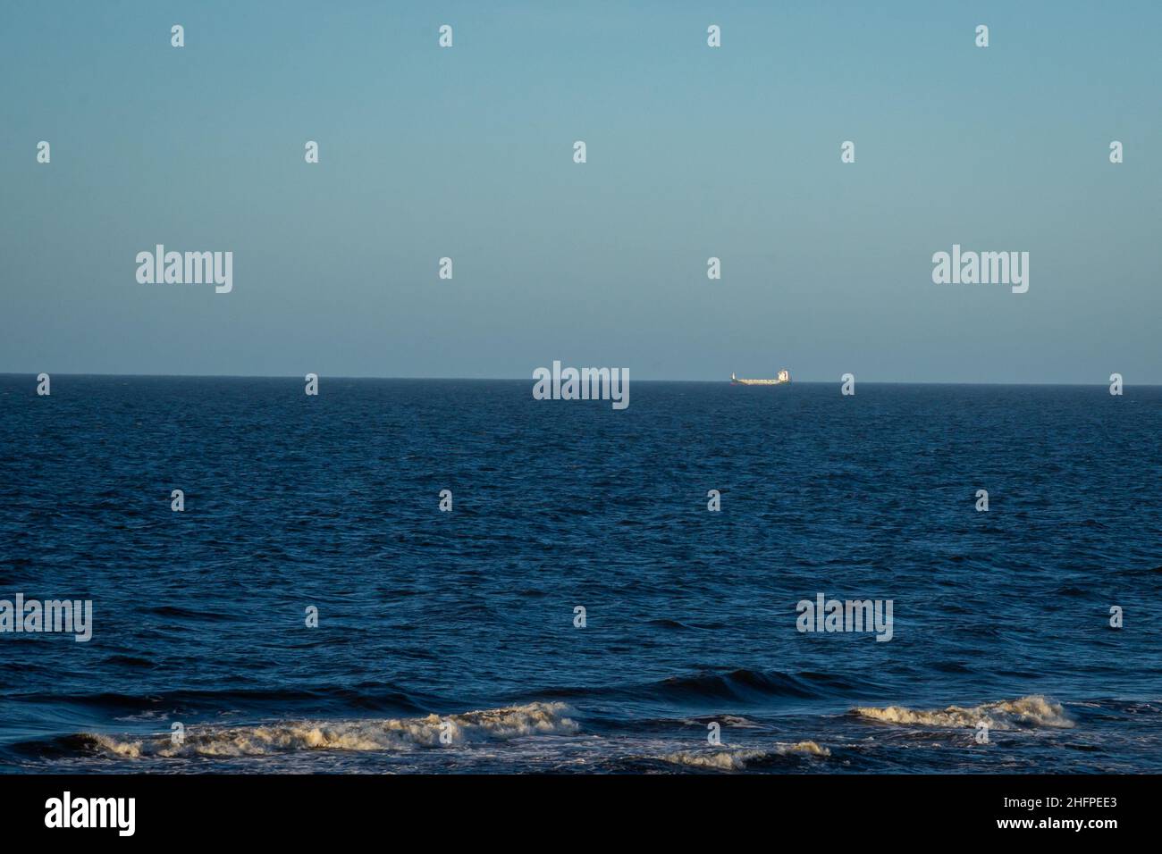 Paysage de mer avec eau bleue et vagues avec mousse blanche.Un navire de transport peut être vu à la distance à l'horizon. Banque D'Images