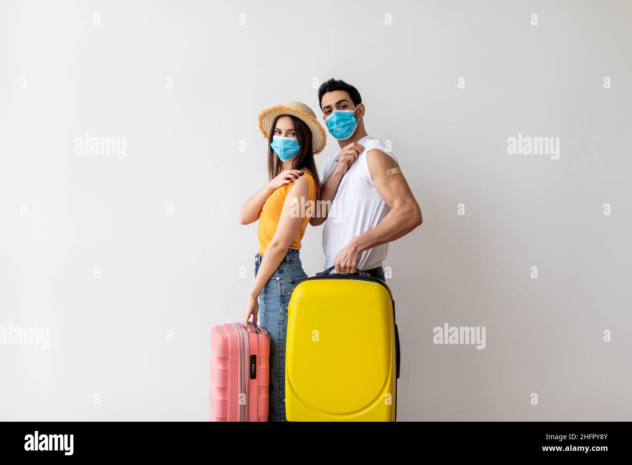 Jeune couple prêt pour un voyage de vacances d'été sûr, tenant des valises et montrant des armes après avoir reçu le vaccin Covid-19 Banque D'Images