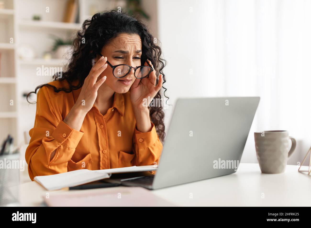 Femme avec une mauvaise vue portant des lunettes regardant un ordinateur portable à l'intérieur Banque D'Images
