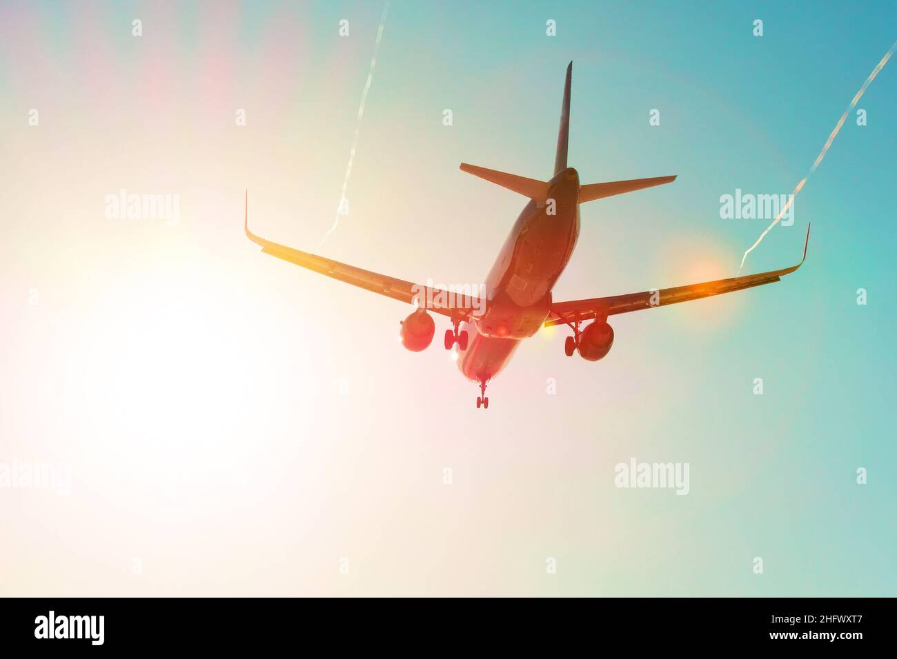 L'avion passager vole près de l'éblouissement solaire avec un dégradé de couleur arc-en-ciel à l'atterrissage, avec les ailes d'un vortex à jet de vapeur Banque D'Images