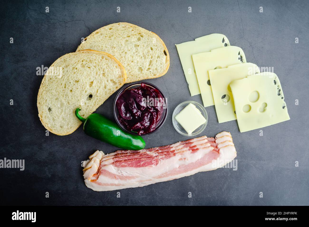 Sandwich au fromage grillé au bacon mûr Ingrédients : vue de dessus du pain au levain, du bacon cru et d'autres ingrédients sur fond sombre Banque D'Images Sandwich au fromage grillé au bacon mûr Ingrédients : vue de dessus du pain au levain, du bacon cru et d'autres ingrédients sur fond sombre Banque D'Images