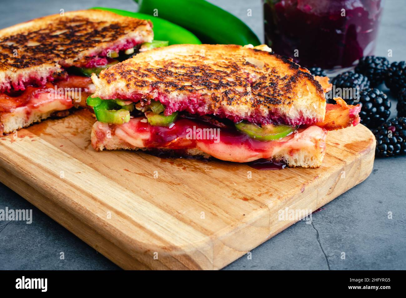 Sandwich au bacon grillé au fromage : sandwich grillé sur du pain au levain recouvert de fromage suisse, confiture de mûres, poivrons jalapeno et bacon Banque D'Images Sandwich au bacon grillé au fromage : sandwich grillé sur du pain au levain recouvert de fromage suisse, confiture de mûres, poivrons jalapeno et bacon Banque D'Images