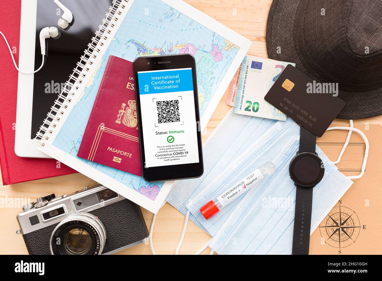 Vue de dessus de quelques accessoires de voyage, un téléphone portable avec le certificat numérique de vaccination et plusieurs masques faciaux sur une table en bois.Paspapo Covid Banque D'Images
