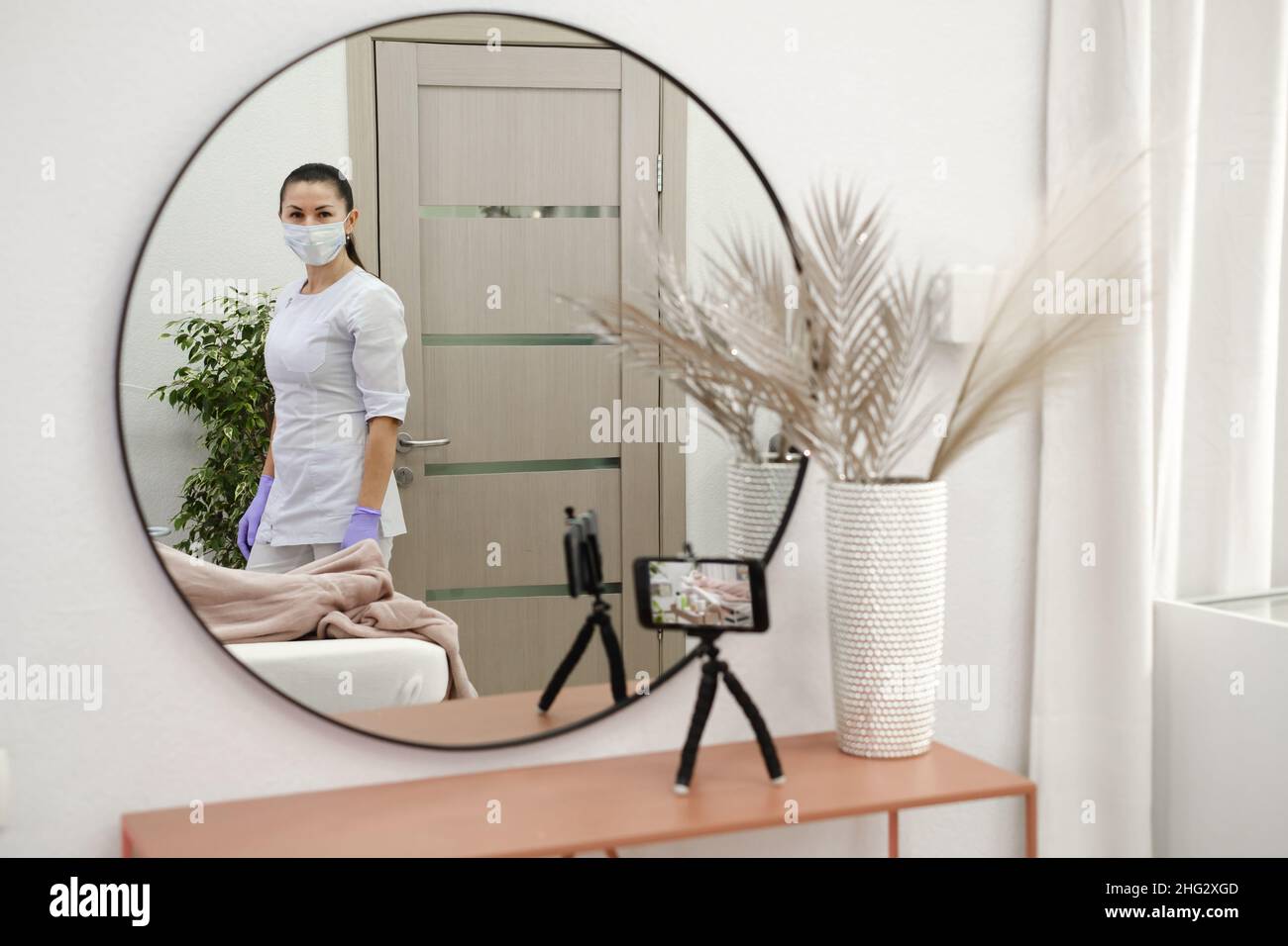 Cosmetologiste dans le bureau du médecin, voir par le miroir et le smartphone en streaming de la procédure de beauté dans la clinique esthétique.Un blogueur dermatologue créatif Banque D'Images