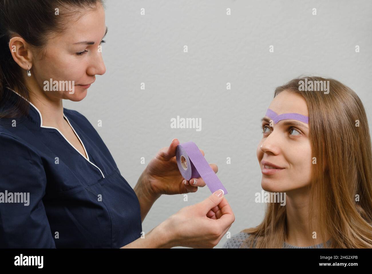 une esthéticienne féminine qui fait le maquillage kinésio du visage.Rayures violettes sur le front contre les rides et le vieillissement Banque D'Images une esthéticienne féminine qui fait le maquillage kinésio du visage.Rayures violettes sur le front contre les rides et le vieillissement Banque D'Images