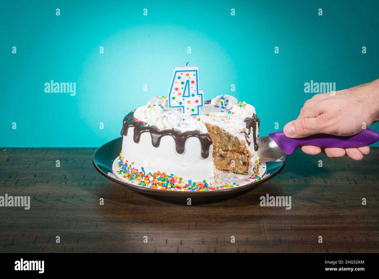 Un gâteau d'anniversaire, manquant une tranche, porte une bougie en forme de numéro 4 tandis qu'une main coupe une autre tranche. Banque D'Images