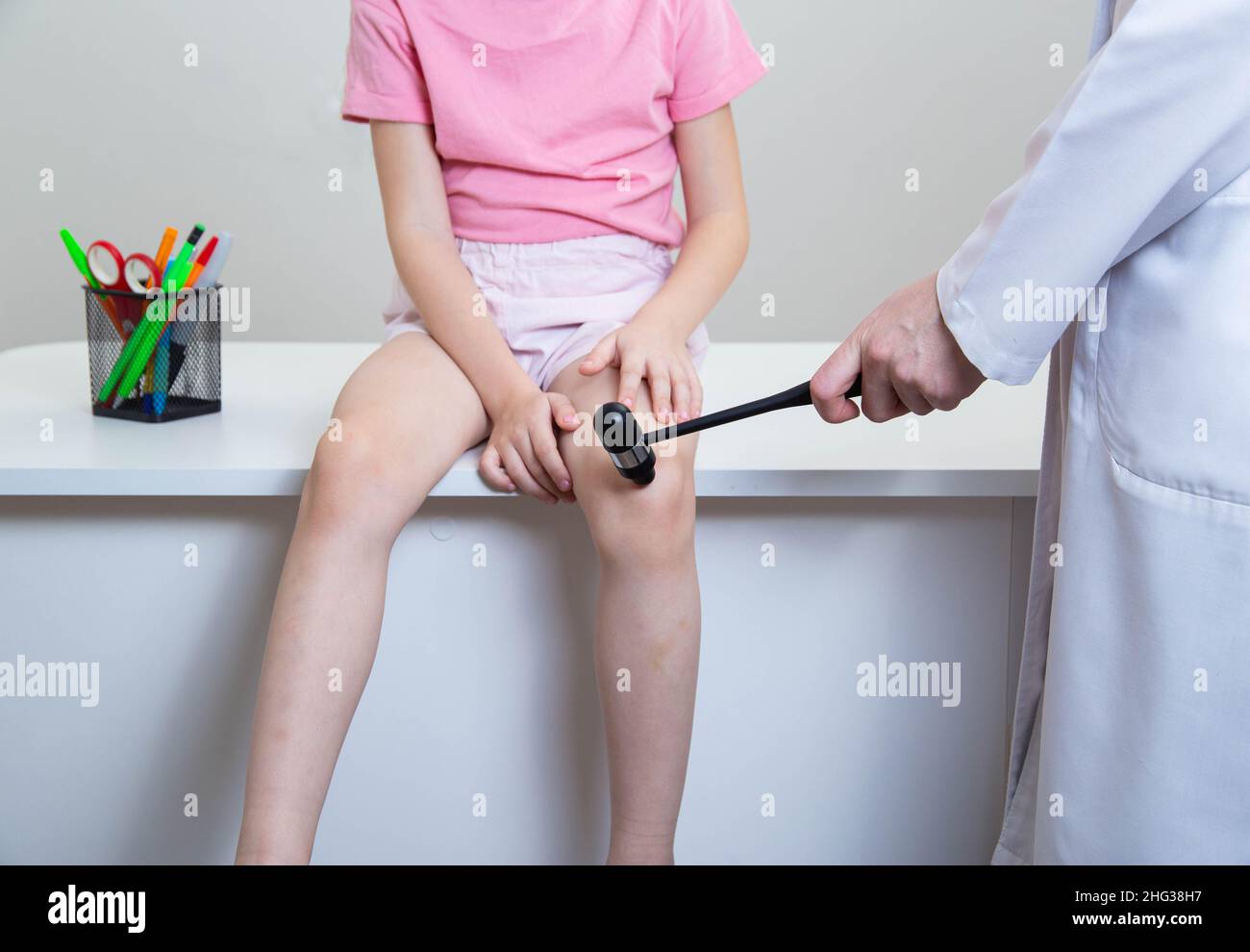 Le médecin neuropathologiste vérifie le réflexe du genou de l'enfant, frappe avec un marteau neurologique. Banque D'Images