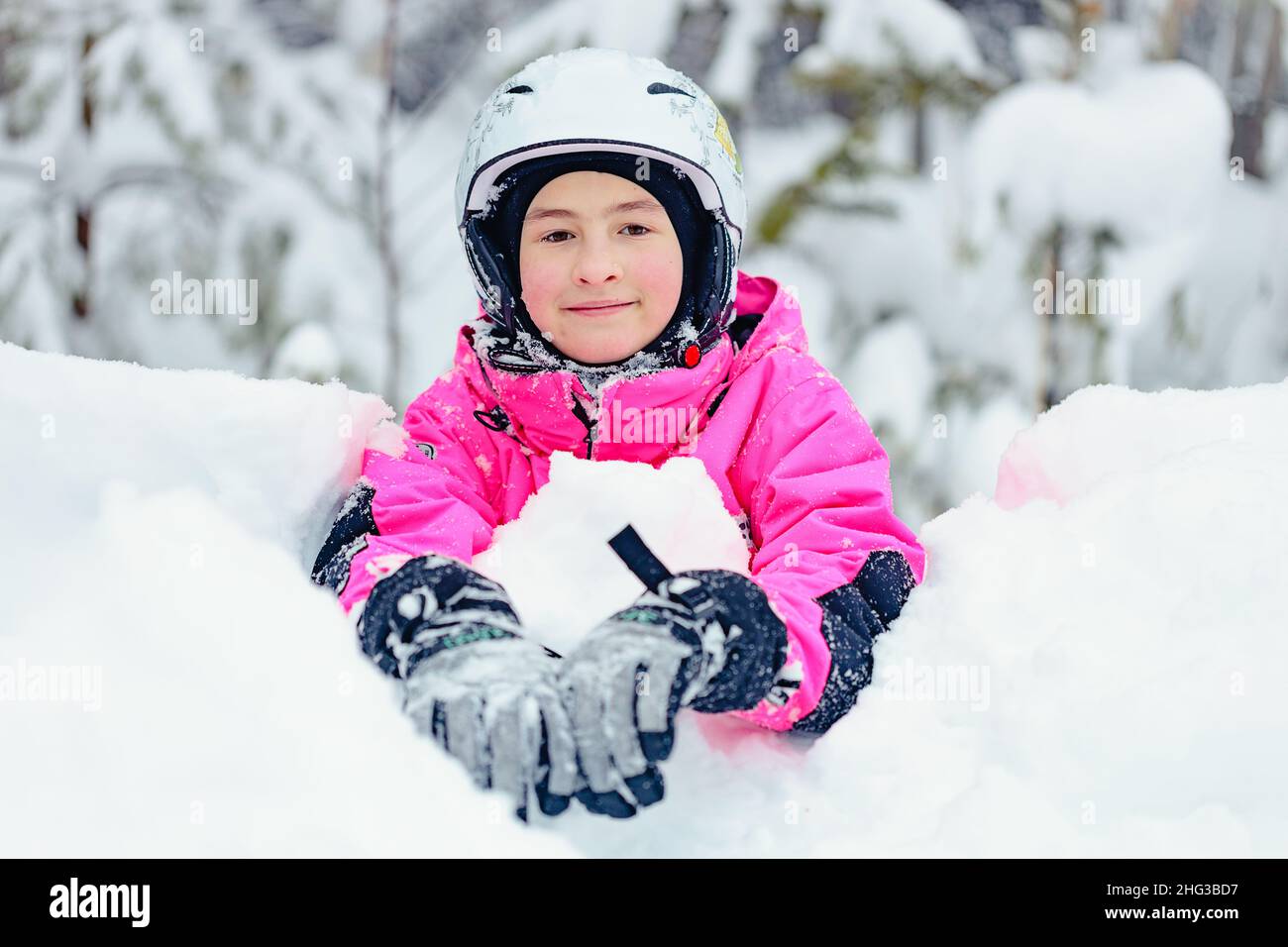 Adorable bonbonne de neige de fille dans des vêtements d'hiver lumineux passe du temps dans un parc de snowboard enneigé.Fille souriante d'origine caucasienne sur l'hiver en plein air recr Banque D'Images