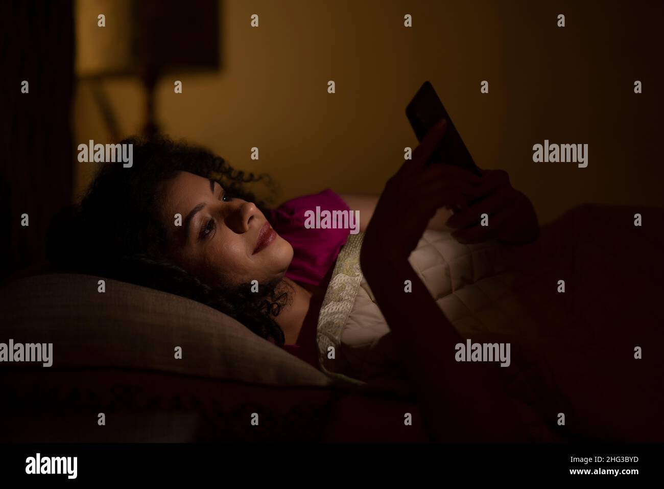 Femme discutant sur smartphone la nuit en étant couché sur le lit Banque D'Images