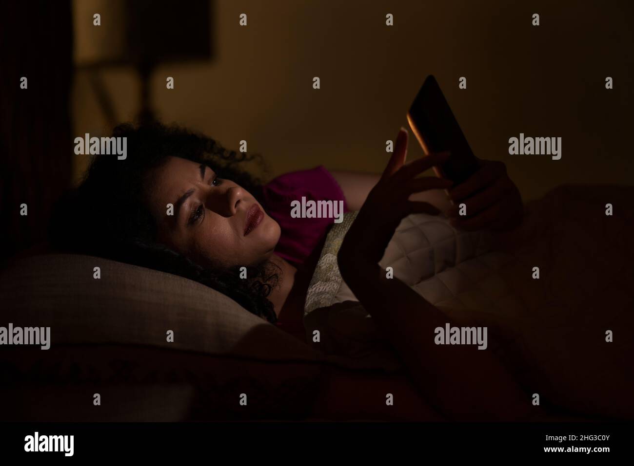 Femme discutant sur smartphone la nuit en étant couché sur le lit Banque D'Images