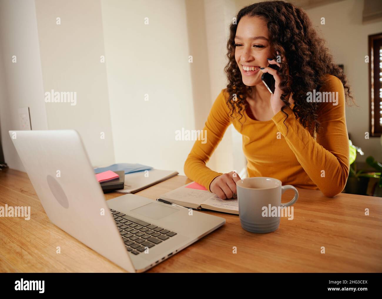 Femme afro-américaine parlant sur un appareil cellulaire lors d'un appel professionnel à l'aide d'un ordinateur portable Banque D'Images