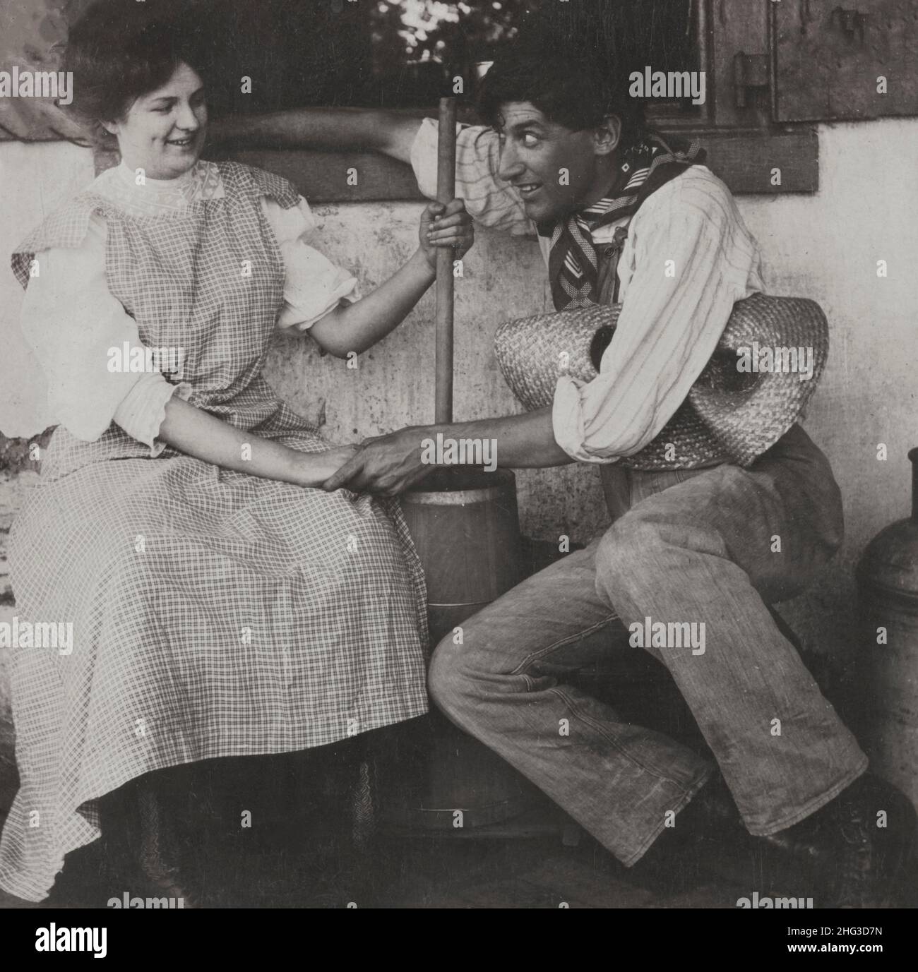 Photo d'amour vintage.Juste en attendant le babeurre.ÉTATS-UNIS.1906 Farmer tenant la main de la femme qui est beurre de churning. Banque D'Images