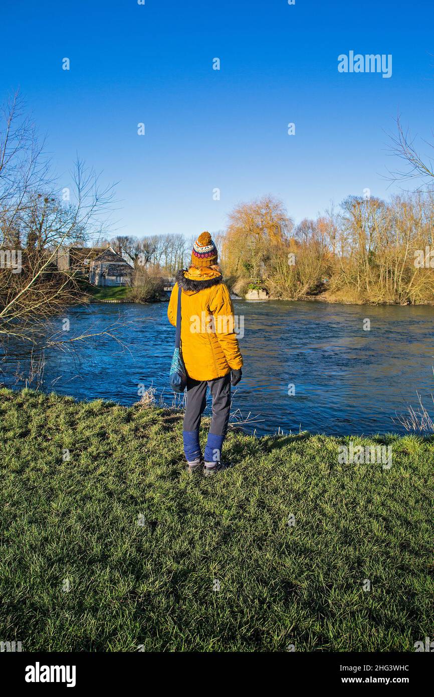 Une femme portant une veste jaune vif et un chapeau est debout et regarde l'écluse de Buscot sur la Tamise lors d'une journée d'hiver lumineuse et ensoleillée Banque D'Images