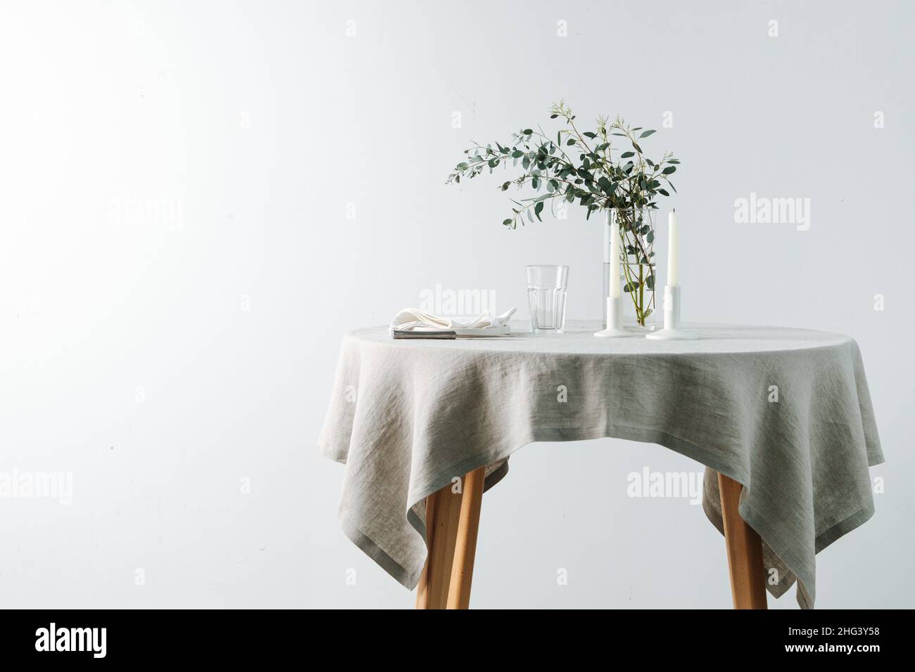 Table ronde avec nappe blanche décorée de bougies et branche décorative.Sur un mur blanc. Banque D'Images