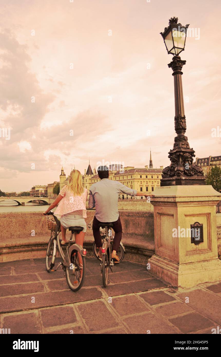 Couple en vélo regardant le coucher du soleil sur Paris et la Seine depuis le Pont neuf, scène romantique dans la ville française de l'amour Banque D'Images
