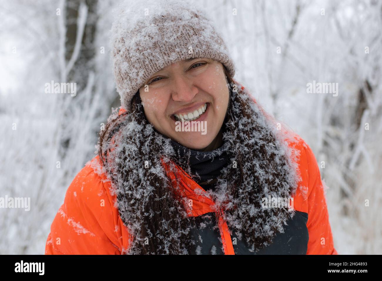 Portrait d'une femme d'âge moyen en riant avec les yeux regardant l'appareil photo vêtu de vêtements chauds d'hiver avec les cheveux et le chapeau recouvert de neige.Bel hiver Banque D'Images